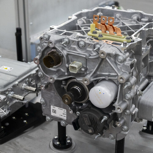 Two electric vehicle powertrain components: a larger motor or gearbox with connectors on the right, and a smaller inverter or control unit with electrical ports on the left, both mounted on a platform.